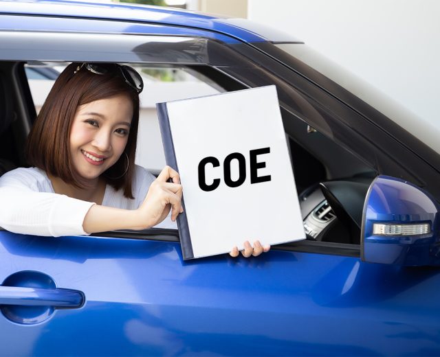 Woman in blue car holding up certificate of entitlement (COE) in Singapore