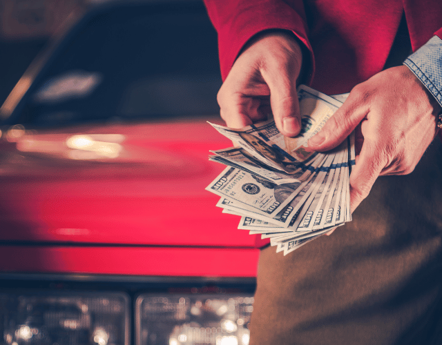 Close-up of a man counting his money in front of his red car